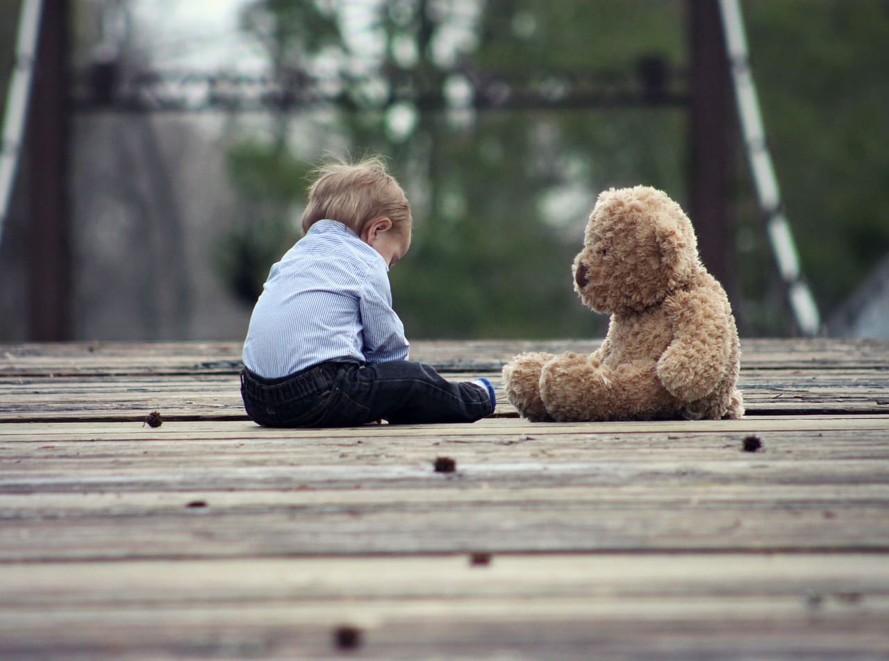 Un enfant jouant seul, de dos, à côté de son nounours